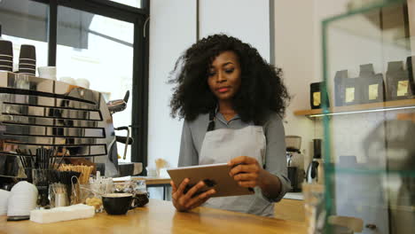 African-american-female-barista-with-curly-hair-using-a-tablet-in-a-coffee-shop