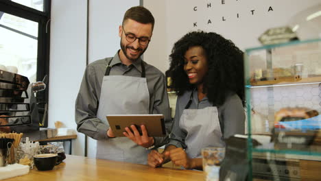 Two-young-barista-man-and-woman-using-tablet-computer-during-a-break-in-a-coffee-shop