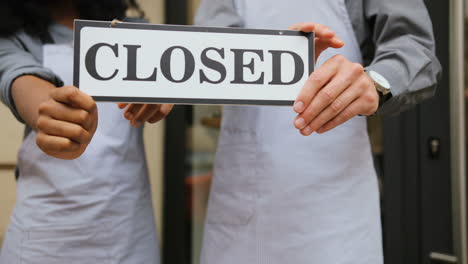 Close-up-view-of-caucasian-waiter-and-african-waitress-hands-holding-a-signboard-closed"-outside-of-coffee-shop"