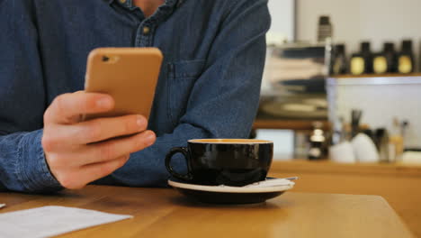 Close-up-view-of-african-female-waiter-hands-serving-a-cup-of-coffee-to-young-caucasian-man-who-is-using-a-smartphone