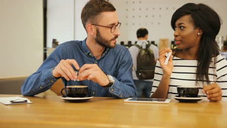 Young-caucasian-man-in-glasses-drinking-coffee-with-african-american-woman-in-a-modern-coffee-shop