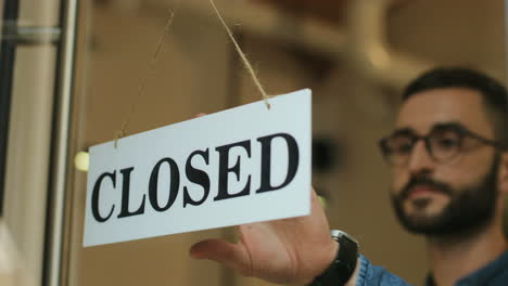 Close-up-view-of-young-man-turning-over-a-open"-signboard-in-coffee-shop-door"