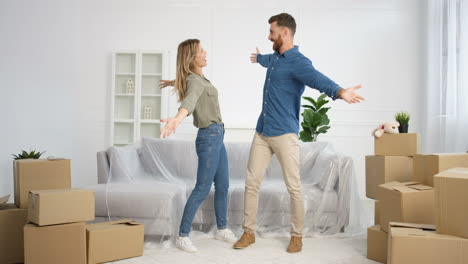 Caucasian-young-cheerful-married-couple-having-fun,-laughing-and-jumping-in-living-room-among-carton-boxes