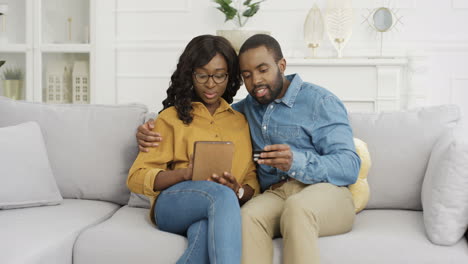 Afroamerikanisches-Junges-Glückliches-Paar,-Das-Auf-Dem-Sofa-Sitzt-Und-Online-Mit-Tablet-Und-Kreditkarte-Einkauft