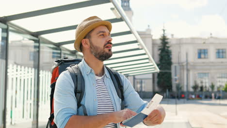 Young-handsome-Caucasian-traveller-wearing-hat-with-backpack-watching-passport-and-ticket-in-the-street