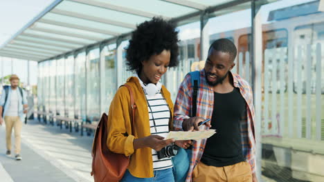 African-American-young-couple-of-tourists-walking-with-map-and-looking-for-right-route-in-bus-station