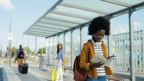 Young-african-american-female-traveller-with-backpack-holding-city-map-while-walking-at-bus-station
