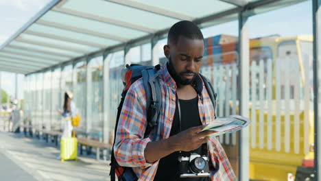 Young-african-american-traveller-with-backpack-holding-city-map-while-walking-at-bus-station