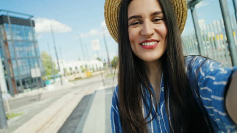 Close-up-view-of-Caucasian-young-happy-woman-traveller-in-hat-talking,-waving-hands-and-smiling-at-the-camera-outdoors-in-summer