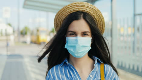 Portrait-of-young-caucasian-traveller-woman-wearing-medical-mask-and-hat-looking-at-camera-outdoors