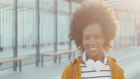 Close-up-view-of-african-american-woman-traveller-in-headphones-smiling-and-looking-at-camera-at-bus-station