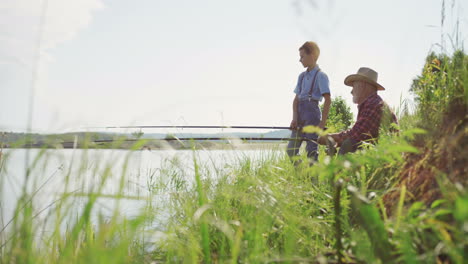 Cute-teen-boy-spending-good-time-inthe-nature-with-his-grandpa-while-they-ar-angling-in-a-lake