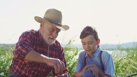 Portrait-of-grandson-with-his-grandfather-taking-off-a-fish-from-a-rod-after-catching-it-from-the-lake