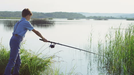 Teen-boy-fishing-on-the-picturesque-lake-shore-with-a-big-rod-in-the-morning-on-a-summer-day