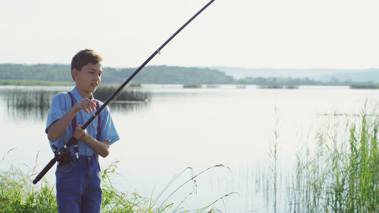 Free stock video - Teen boy fishing on the lake and catching a fish with  the rod