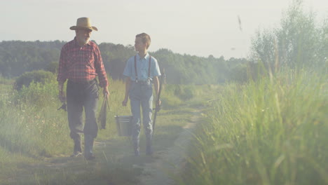 Caucasian-grandfather-and-his-little-grandson-walking-together-while-holding-fishing-rods-in-the-morning