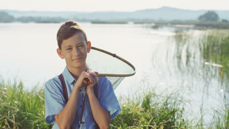 Portrait-of-the-nice-teenage-boy-standing-with-a-scoop-net-and-smiling-at-the-camera