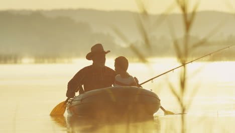 Senior-fisherman-in-hat-floating-with-his-grandson-in-the-boat-and-fishing-with-a-rod-in-the-lake