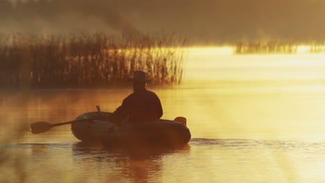 Rückansicht-Eines-älteren-Mannes-Mit-Hut,-Der-Bei-Sonnenuntergang-In-Einem-Boot-Auf-Dem-See-Segelt