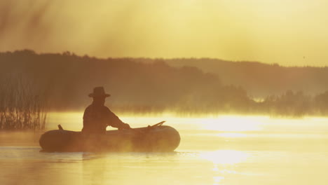 Distant-view-of-senior-man-in-a-hat-sailing-in-a-boat-on-the-lake-at-sunset