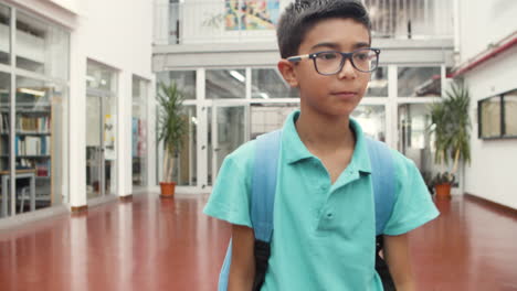 Medium-shot-of-smiling-boy-in-eyeglasses-walking-in-school-corridor,-looking-around-and-at-the-camera