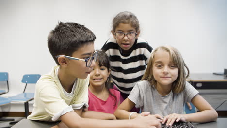 Boy-and-girl-typing-together-on-keyboard-while-two-classmates-watching-at-the-monitor
