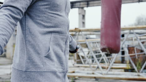 Close-up-view-of-caucasian-man-with-a-beard-in-a-grey-hoodie-jumping-rope-outdoors-an-abandoned-factory-on-a-cloudy-morning