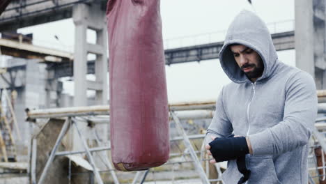 Caucasian-man-wrapping-his-hand-with-black-cloth-and-preparing-for-boxing-outdoors-an-abandoned-factory-on-a-cloudy-morning