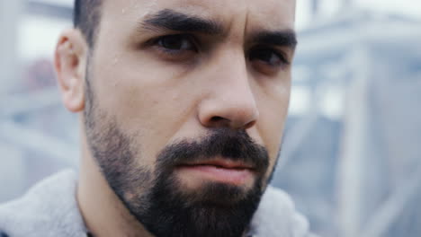 Close-up-view-of-the-sweaty-face-of-bearded-sportsman-during-a-training-outdoors-an-abandoned-factory-on-a-cloudy-morning