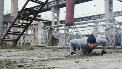 Handsome-male-boxer-doing-push-ups-before-boxing-training-outdoors-the-abandoned-factory-on-a-cloudy-morning
