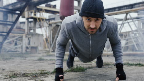 Handsome-male-boxer-wearing-beanie-doing-push-ups-before-boxing-training-outdoors-the-abandoned-factory-on-a-cloudy-morning