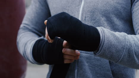 Close-up-view-of-young-male-boxer-wrapping-his-hands-with-black-cloth-outdoors-an-abandoned-factory-on-a-cloudy-morning