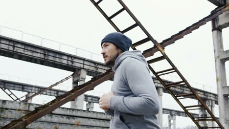 Side-view-of-a-young-sportsman-in-grey-hoodie-jogging-in-a-old-factory-ruins-on-a-cloudy-morning