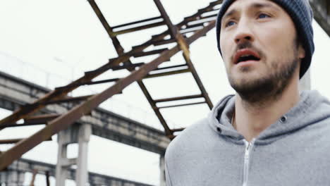 Close-up-view-of-a-young-sportsman-in-grey-hoodie-jogging-in-a-old-factory-ruins-on-a-cloudy-morning