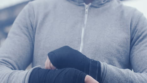 Close-up-view-of-sportsman-wrapping-his-hands-with-black-cloth-on-a-cloudy-morning