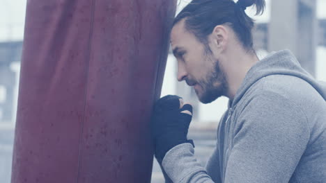 Close-up-view-of-caucasian-man-with-long-hair-hitting-a-punching-bag-outdoors-an-abandoned-factory-on-a-cloudy-morning