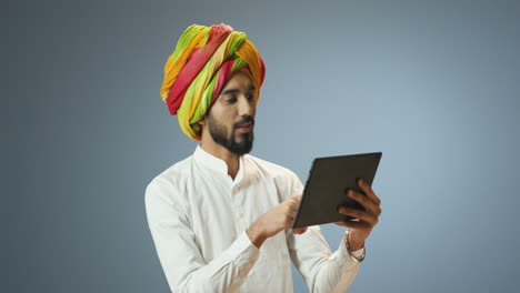 Young-cheerful-Indian-man-in-traditional-clothes-and-turban-making-a-video-call-using-a-tablet