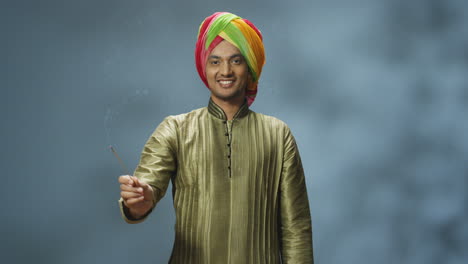 Junger-Glücklicher-Indischer-Mann-In-Turban-Und-Traditioneller-Kleidung,-Der-In-Die-Kamera-Lächelt-Und-Räucherstäbchen-Hält