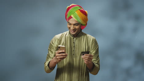 Schöner,-Fröhlicher-Indischer-Mann-In-Turban-Und-Traditioneller-Kleidung,-Der-Online-Mit-Smartphone-Einkauft,-Dann-Lacht-Und-Feiert-Er