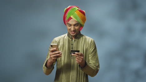 Schöner-Fröhlicher-Indischer-Mann-In-Turban-Und-Traditioneller-Kleidung,-Der-Online-Mit-Smartphone-Einkauft-Und-In-Die-Kamera-Lächelt