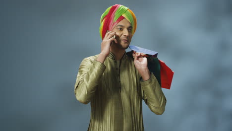 Junger-Fröhlicher-Inder-In-Traditioneller-Kleidung-Und-Turban,-Der-Am-Telefon-Spricht-Und-Einkaufstüten-Hält