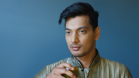 Close-up-view-of-indian-young-man-in-traditional-clothes-drinking-hot-tea-and-looking-at-camera