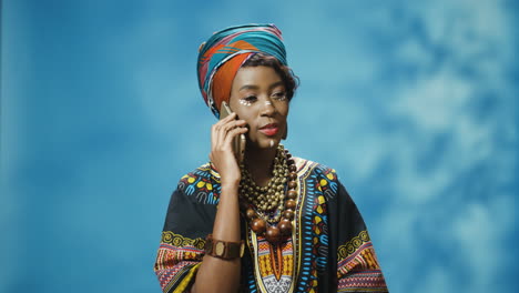 Afroamerikanische-Junge-Schöne-Frau-In-Traditioneller-Kleidung-Und-Turban,-Die-Auf-Dem-Smartphone-Spricht