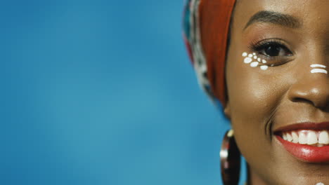 Close-up-view-of-half-face-of-African-American-young-cheerful-woman-in-turban-and-make-up-smiling-joyfully-at-camera