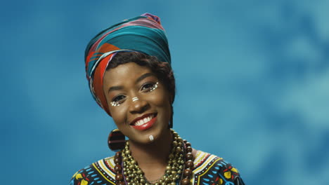 Close-up-view-of-African-American-young-cheerful-woman-in-turban-and-make-up-smiling-joyfully-at-camera