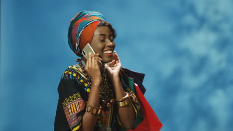 Afroamerikanische-Junge-Frau-In-Turban-Und-Traditioneller-Kleidung,-Die-Am-Telefon-Spricht-Und-Einkaufstüten-Hält
