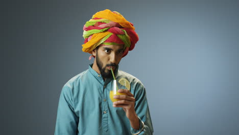 Junger-Fröhlicher-Indischer-Mann-In-Traditioneller-Kleidung-Und-Turban,-Der-Orangensaft-Trinkt-Und-In-Die-Kamera-Schaut