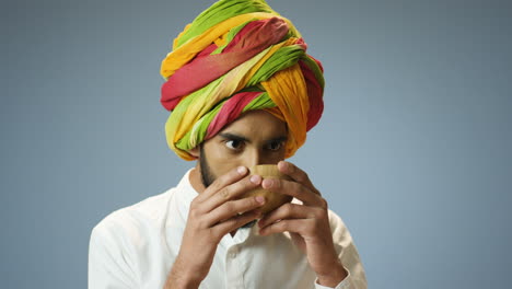 Close-up-view-of-young-cheerful-Indian-man-in-traditional-clothes-and-turban-drinking-tea-from-a-cup