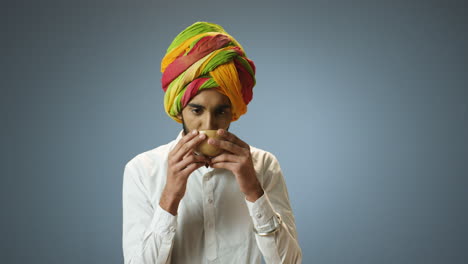 Young-cheerful-Indian-man-in-traditional-clothes-and-turban-drinking-tea-from-a-cup