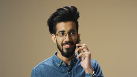 Junger-Hübscher-Inder-Mit-Bart-Und-Brille,-Der-Fröhlich-Am-Handy-Spricht-Und-Lächelt